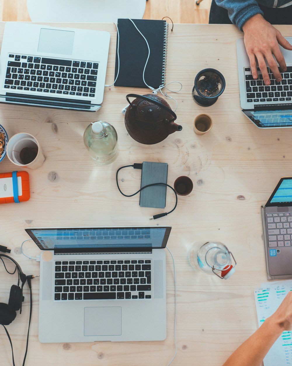 Overhead view of a team's shared desk covered in open laptops, phones and coffee during a work session